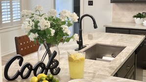 A kitchen with a marble countertop, a black faucet, a chandelier, and a bowl of lemons. - 3 mi to Kyle Field, Farm house Ranchette, sleeps 20! (College Station)