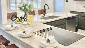 A modern kitchen with a central island, a chandelier, and a dining area with brown leather chairs. - 3 mi to Kyle Field, Farm house Ranchette, sleeps 20! (College Station)