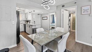Een moderne keuken met witte kasten, een eetgedeelte met een tafel met glazen blad en een bijzondere ronde lamp.