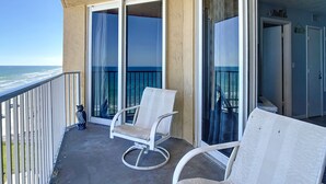 A balcony with two white chairs, a view of the ocean, and a door to the right. - Direct Oceanfront Condo - Pool, Beach & Steps from Flagler Ave (New Smyrna Beach)