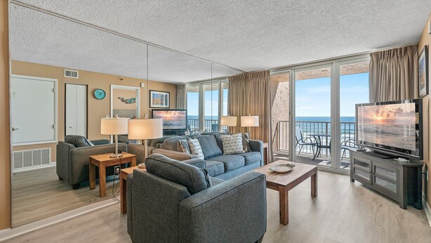 Un salon spacieux avec un grand canapé, une table basse et un téléviseur. Il y a un balcon avec vue sur l’océan.