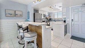 Una cocina moderna con armarios blancos, una isla central con taburetes y un refrigerador.