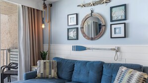 Una sala de estar moderna con un sofá azul, almohadones decorativos, un espejo montado en la pared, obras de arte enmarcadas y una decoración con forma de estrella de mar.