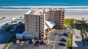 A high-rise hotel with a beach view, parking lot, and a pool area.