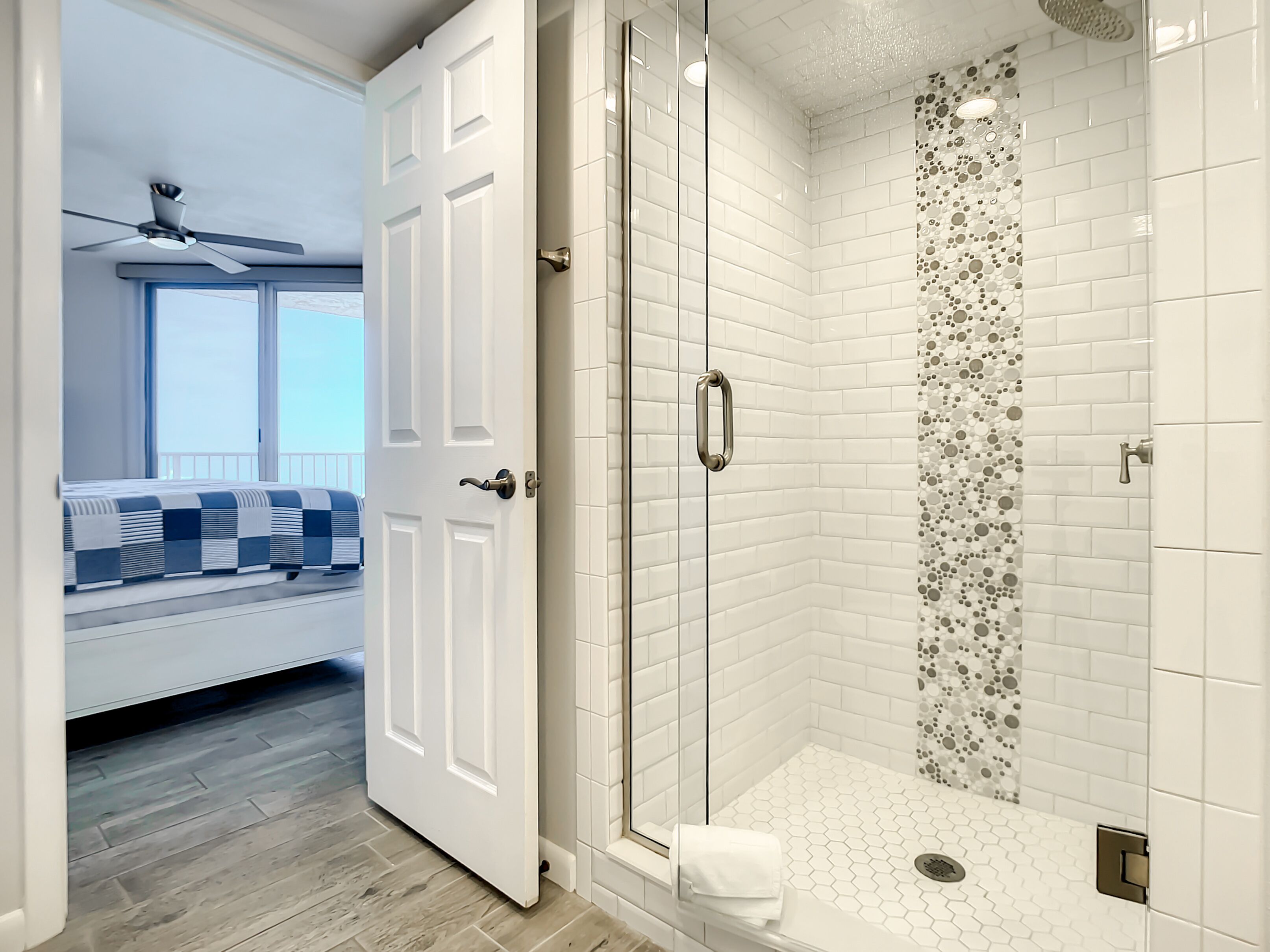 Une salle de bain moderne avec une douche à parois de verre, des carreaux de céramique blancs rectangulaires et un mur décoratif en mosaïque.