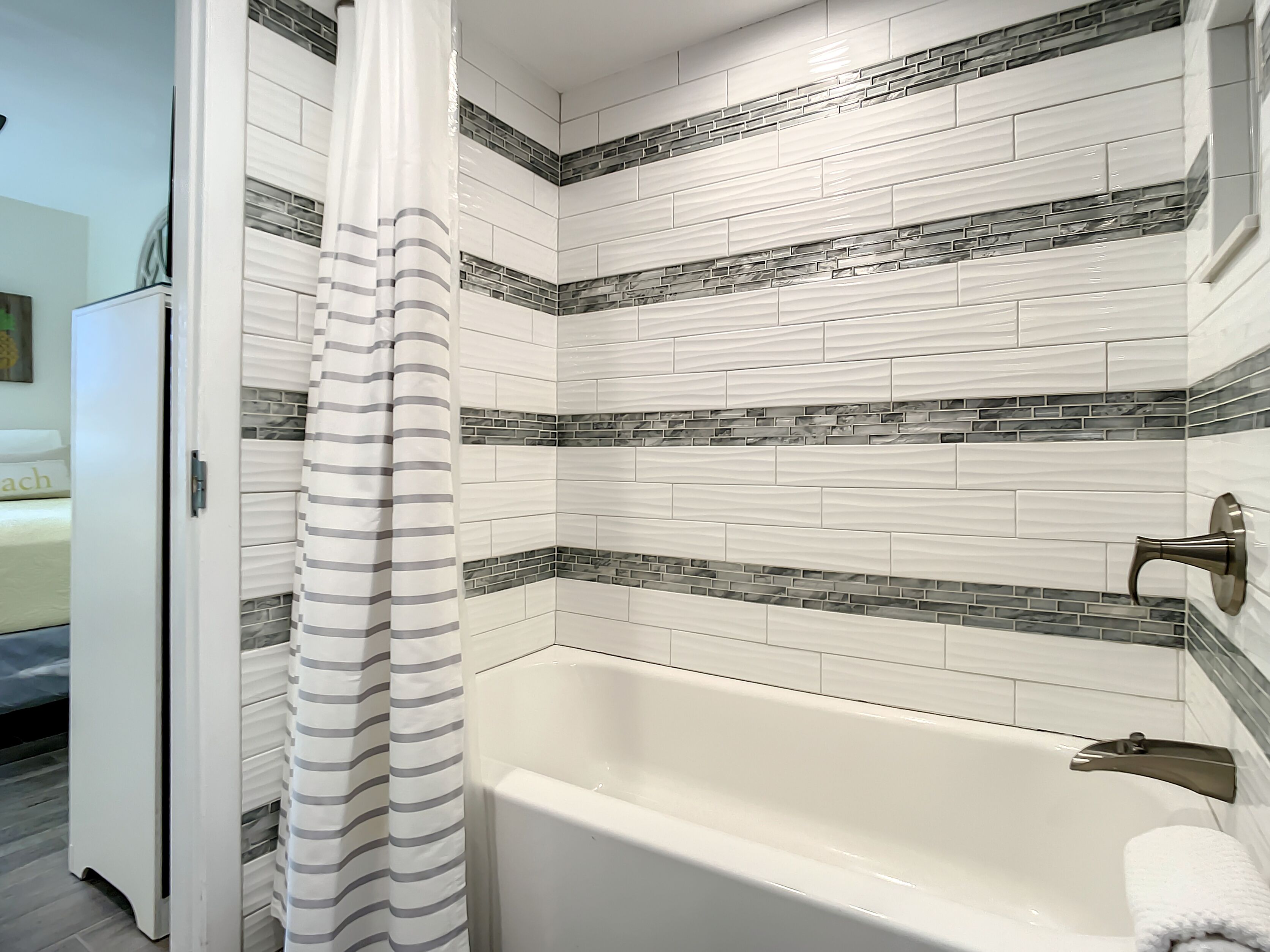 A bathroom with a white bathtub, striped shower curtain, and tiled walls with a brick pattern accent.