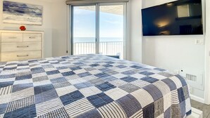 Une chambre dotée d’un grand lit, d’un ventilateur de plafond, d’un téléviseur fixé au mur et d’une porte-fenêtre coulissante donnant sur un balcon avec vue sur l’océan.