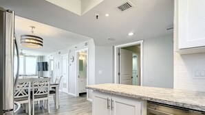 A modern kitchen with white cabinetry, a marble countertop, and a dining area with a wooden table and chairs.
