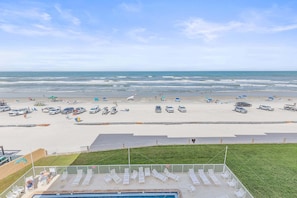 A beach view with a pool area, lounge chairs, and umbrellas. - Oceanfront Condo with Pool, BBQ & Steps from Flagler Ave (New Smyrna Beach)