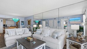 A living room with a white sofa, a coffee table, a TV, and a kitchen in the background.
