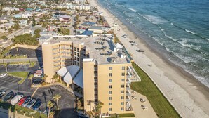 A coastal hotel with multiple floors, a parking lot, and a beach view. - Bright Oceanview Condo • Steps to Sand & Flagler Dining Scene (New Smyrna Beach)