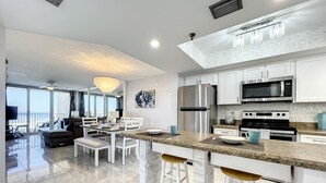 A modern kitchen with white cabinetry, stainless steel appliances, and a bar area with stools. - Bright Oceanview Condo • Steps to Sand & Flagler Dining Scene (New Smyrna Beach)