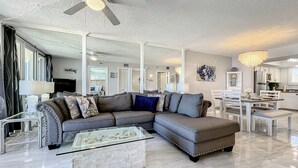 A spacious living room with a sectional sofa, a glass coffee table, and a dining area with white furniture. - Bright Oceanview Condo • Steps to Sand & Flagler Dining Scene (New Smyrna Beach)