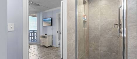 Un baño moderno con cabina de ducha de vidrio, suelo de baldosas y lavamanos a la vista.