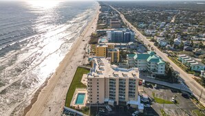 An aerial view of a coastal hotel with a pool, multiple buildings, and a beach. - Beachfront, Pool, BBQ & Game room!  Extra Windows = More Light & More Views (New Smyrna Beach)