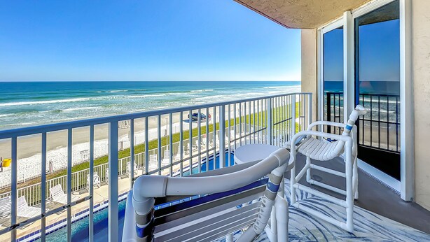 A balcony with a view of the ocean, a pool, and beach chairs. - Beachfront, Pool, BBQ & Game room!  Extra Windows = More Light & More Views (New Smyrna Beach)
