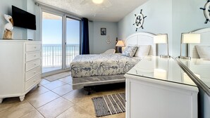 A bedroom with a bed, a dresser, a TV, a ceiling fan, and a view of the ocean. - Beachfront, Pool, BBQ & Game room!  Extra Windows = More Light & More Views (New Smyrna Beach)