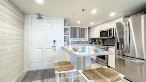 Una cocina moderna con armarios blancos, electrodomésticos de acero inoxidable y una isla central con taburetes de bar.