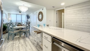 Una cocina moderna con encimera de mármol, armarios blancos y un comedor con candelabro.