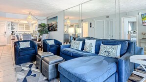 A modern living room with a sofa set, ottomans, and a dining area. - Updated 2BR oceanfront condo with balcony & pool (New Smyrna Beach)