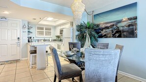 A modern kitchen with white cabinets, a central island, and a dining area with a glass table and chairs. - Updated 2BR oceanfront condo with balcony & pool (New Smyrna Beach)