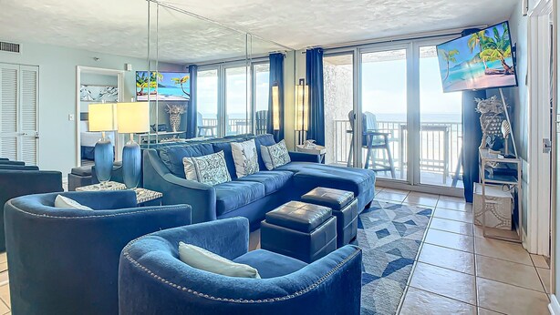 A spacious living room with a large sofa, armchairs, and a coffee table. There is a TV mounted on the wall, and a balcony with a view of the ocean. - Updated 2BR oceanfront condo with balcony & pool (New Smyrna Beach)