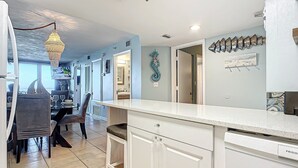 A modern kitchen with white cabinetry, a dining area with a table and chairs, and a decorative seahorse wall hanging. - Updated 2BR oceanfront condo with balcony & pool (New Smyrna Beach)
