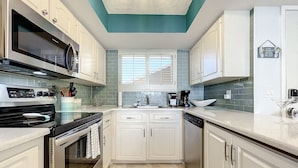 A modern kitchen with white cabinets, a black stove, a microwave, and a dishwasher. - Updated 2BR beachfront condo with balcony + pool (New Smyrna Beach)