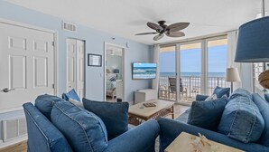 A room with a large window overlooking the sea, a ceiling fan, and a view of the beach. - Updated Oceanfront Condo!  Pool, Beach & steps from Flagler Ave (New Smyrna Beach)