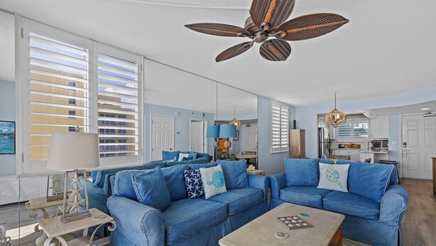 A living room with two blue sofas, a coffee table, and a ceiling fan. - Updated Oceanfront Condo!  Pool, Beach & steps from Flagler Ave (New Smyrna Beach)