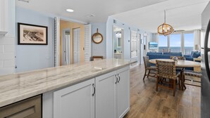 A modern kitchen with white cabinets, a marble countertop, and a dining area with wicker chairs. - Updated Oceanfront Condo!  Pool, Beach & steps from Flagler Ave (New Smyrna Beach)