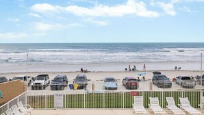 A beach view with a parking area and lounge chairs. - OceanFront Condo - Pool, BBQ, Steps from Flagler Ave (New Smyrna Beach)
