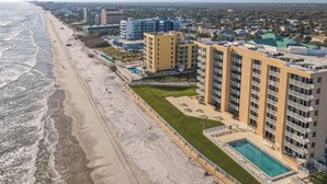 A coastal hotel with multiple floors, a swimming pool, and a beach view.