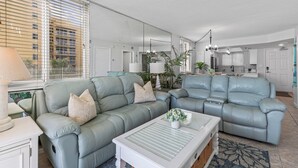 A modern living room with a sectional sofa, a coffee table, and a large window with blinds.