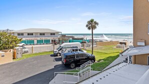 Un’area di parcheggio con un SUV nero, un furgone bianco e un’auto bianca. Si vede un edificio con un’insegna che riporta “Tony & Joe's Patio”. Una palma è visibile e lo sfondo è dato dall’oceano.