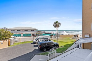 A parking area with a black SUV, a white van, and a white car. There is a building with a sign that reads "Tony & Joe's Patio." A palm tree is visible, and the ocean is in the background.