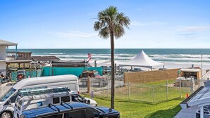 Vista sulla spiaggia con una tenda, una palma e veicoli parcheggiati.