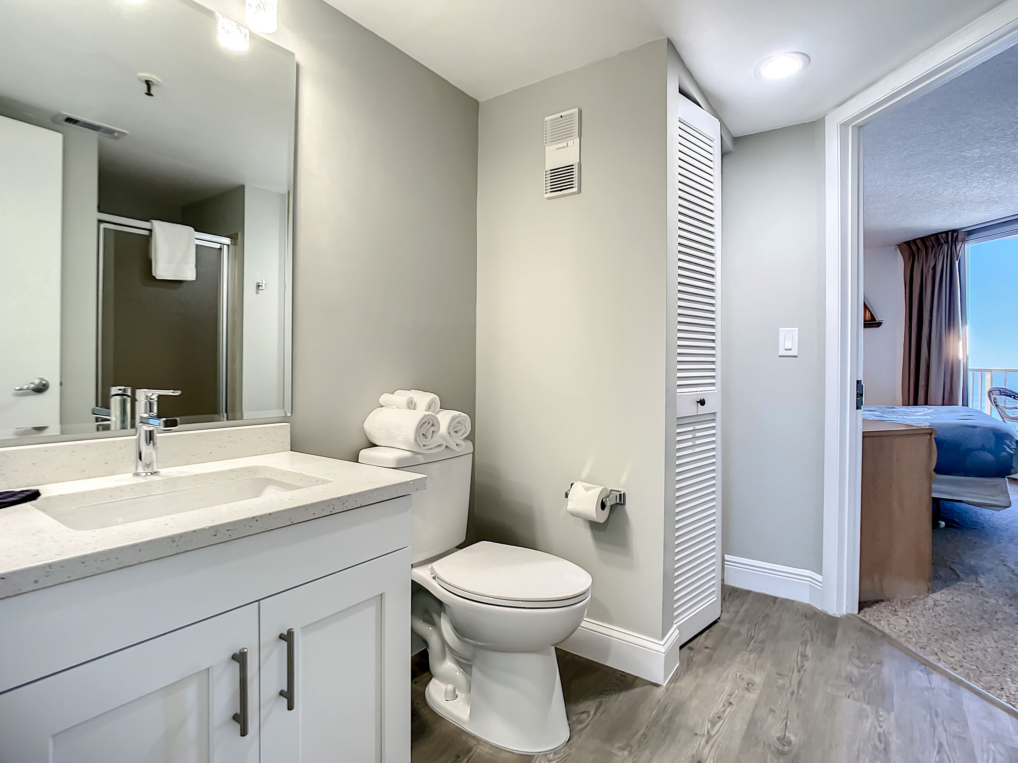 Un bagno moderno con un grande specchio, un lavandino e un water. Ci sono degli asciugamani sul water e si intravede una doccia sullo sfondo.
