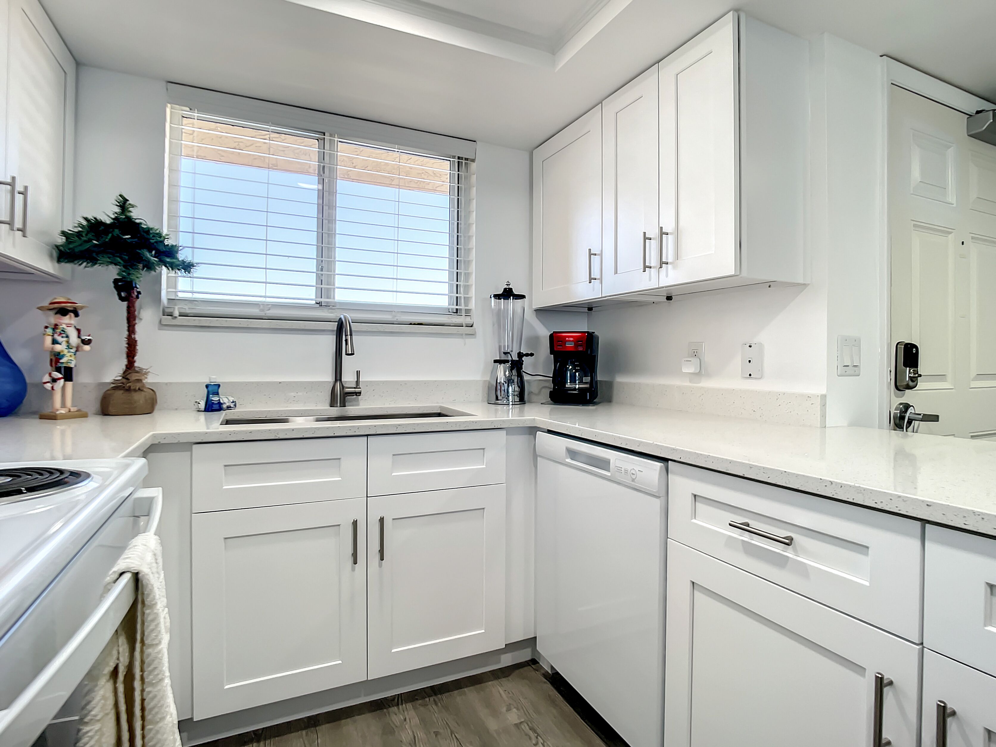 A modern kitchen with white cabinetry, a stainless steel sink, and a coffee maker.