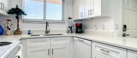 A modern kitchen with white cabinetry, a stainless steel sink, and a coffee maker.