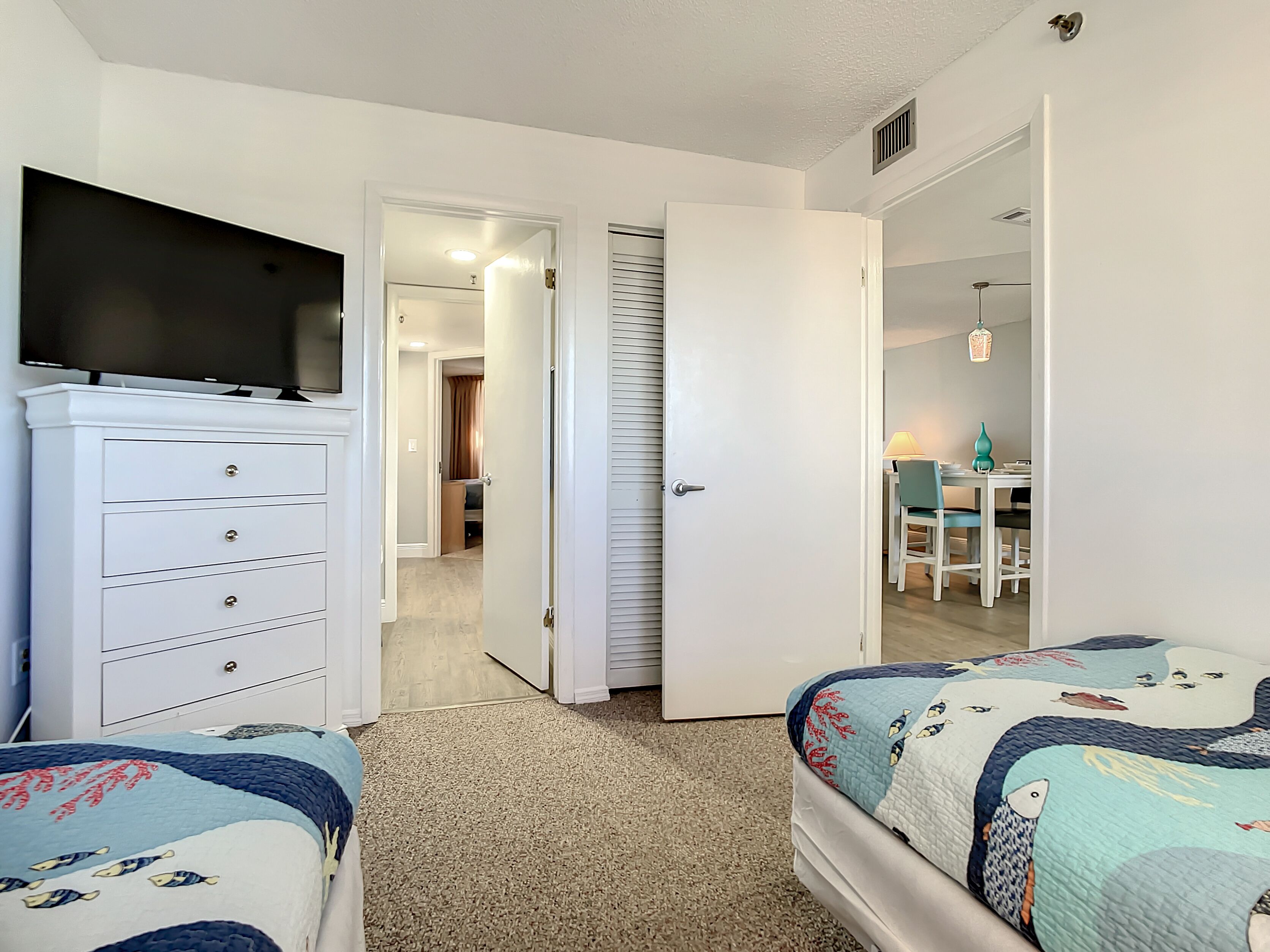 A bedroom with two beds, a TV, a dresser, and a door leading to a bathroom.