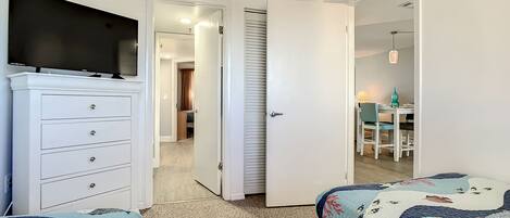 A bedroom with two beds, a TV, a dresser, and a door leading to a bathroom.