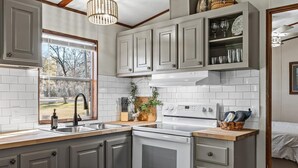 A kitchen with white cabinets, a stainless steel sink, a built-in oven, and a window with a view of trees.