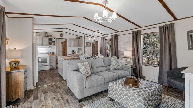 A modern living space with a grey sofa, wooden flooring, and a kitchen in the background.