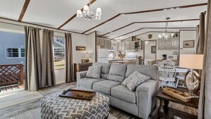A spacious living room with a grey sofa, wooden coffee table, and a chandelier.