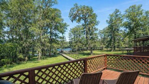 A deck with wicker chairs, a wooden fence, and a view of a lake surrounded by trees.