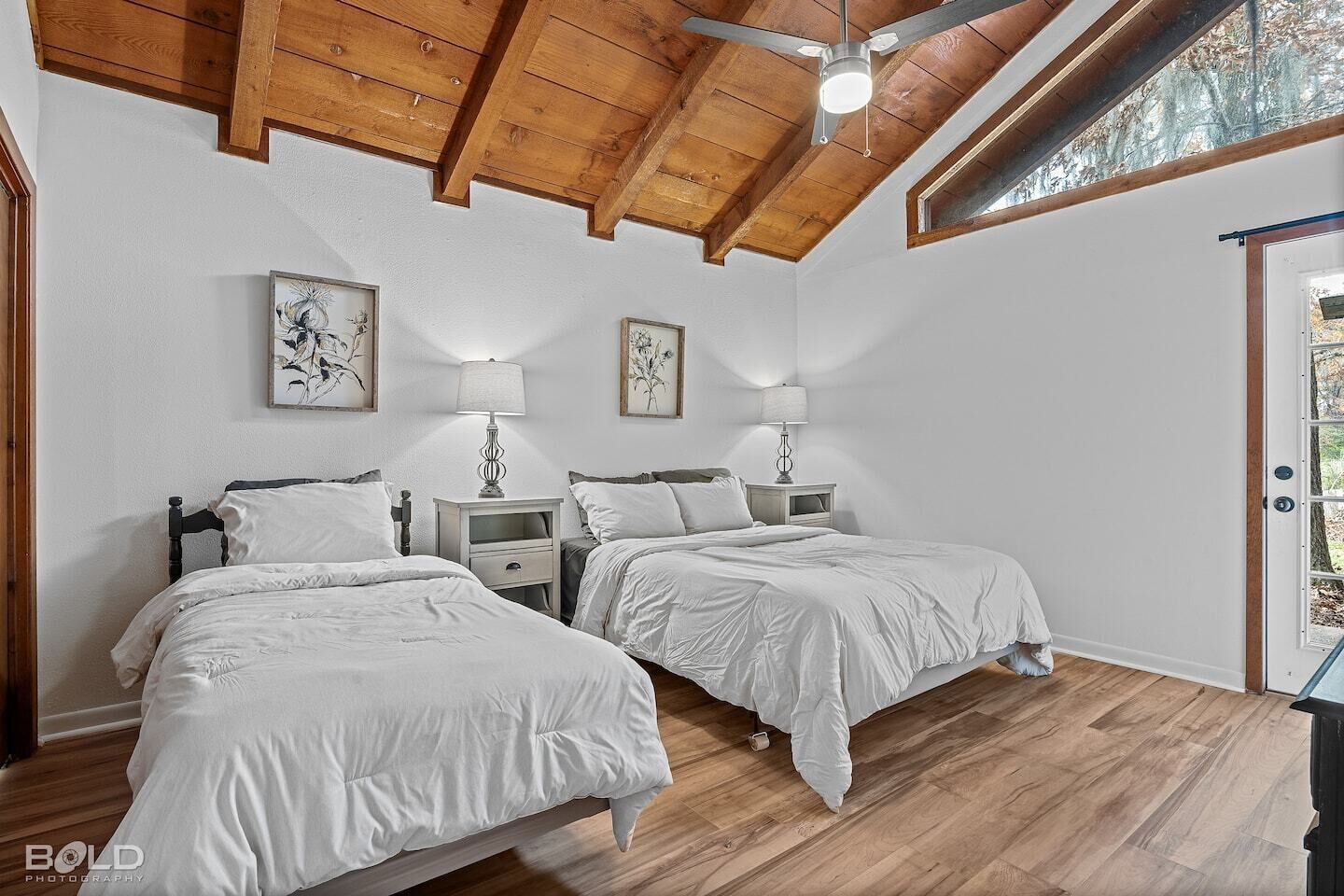 A bedroom with two beds, wooden ceiling beams, and a window.
