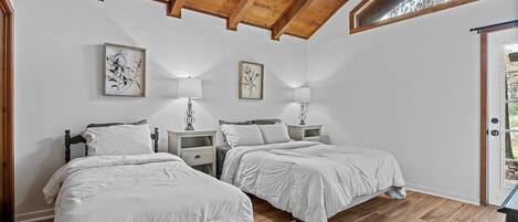 A bedroom with two beds, wooden ceiling beams, and a window.