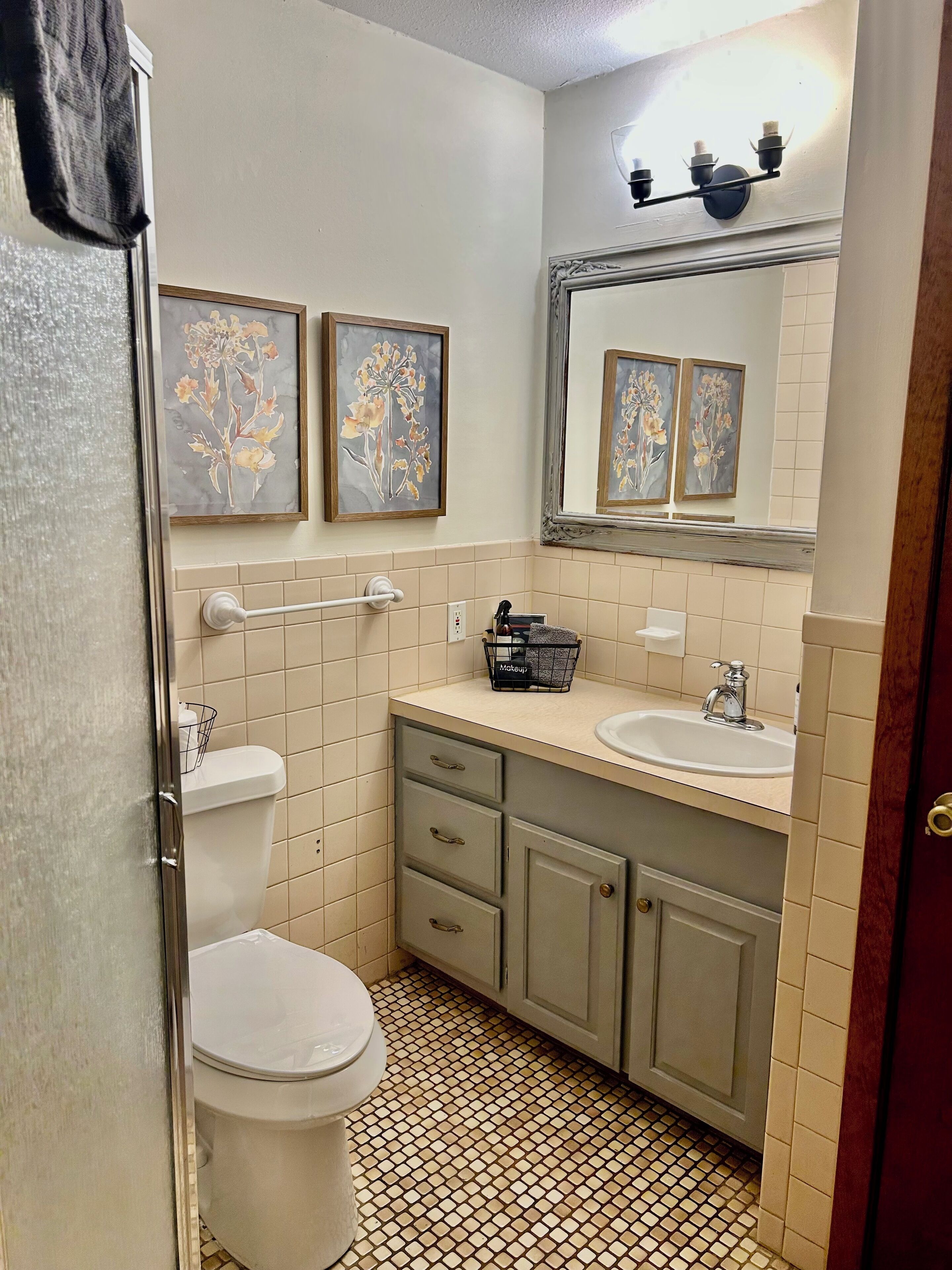 A bathroom with a toilet, sink, and cabinet, featuring a tiled floor and wall-mounted artwork.