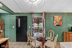 A dining area with a glass table surrounded by wicker chairs, a black door, and a green wall with a painting.